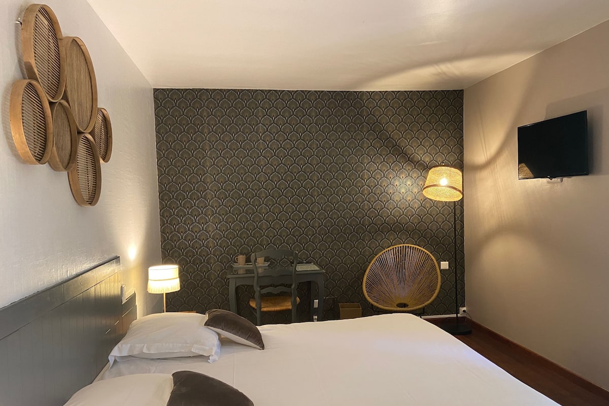 A hotel room with a large bed, a desk, a chair, a television, and a patterned wallpaper.