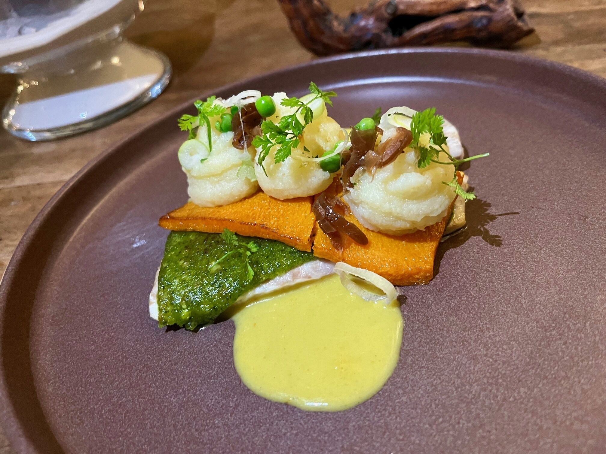 A plate with a dish consisting of a green vegetable, a yellow sauce, and a piece of orange food.