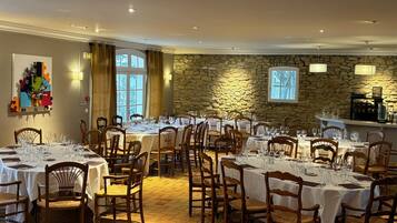 Een restaurant met meerdere ronde tafels gedekt voor diners, stenen muren en een groot raam dat natuurlijk licht binnenlaat.