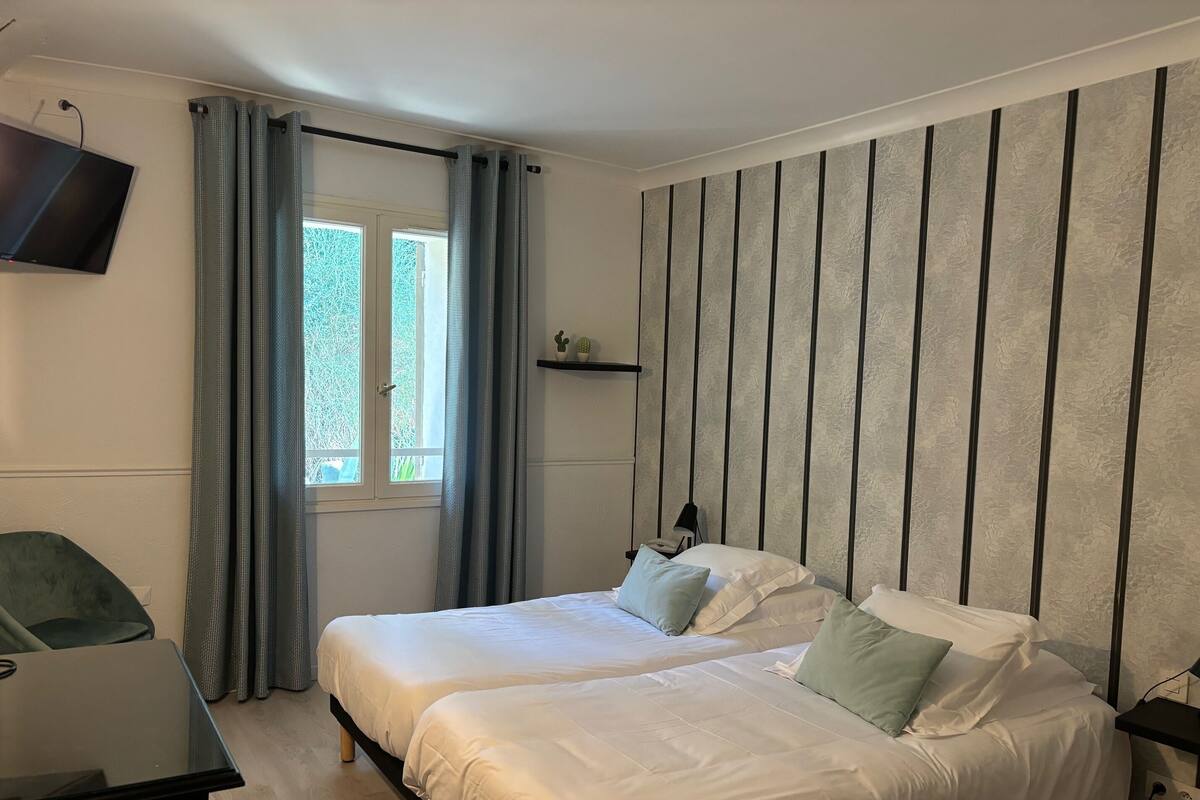 A bedroom with two beds, a TV mounted on the wall, a desk, and a window with curtains.