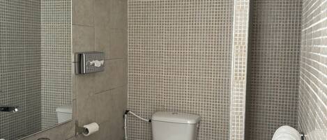 A modern bathroom with a large mirror, a white sink, a toilet, and a shower area.