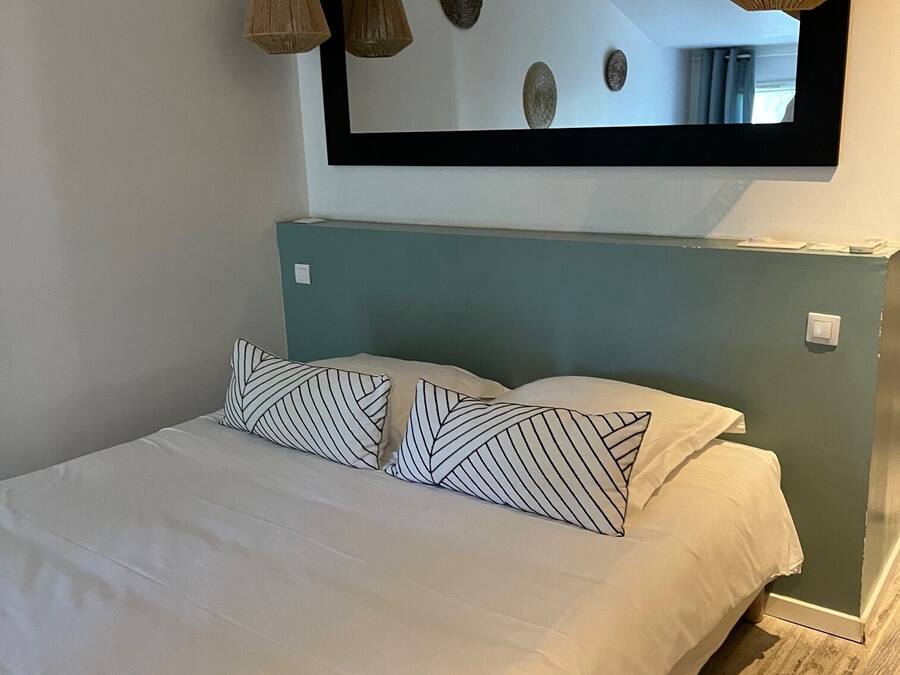 A bed with white bedding and striped pillows, a large mirror above it, and a wooden floor.