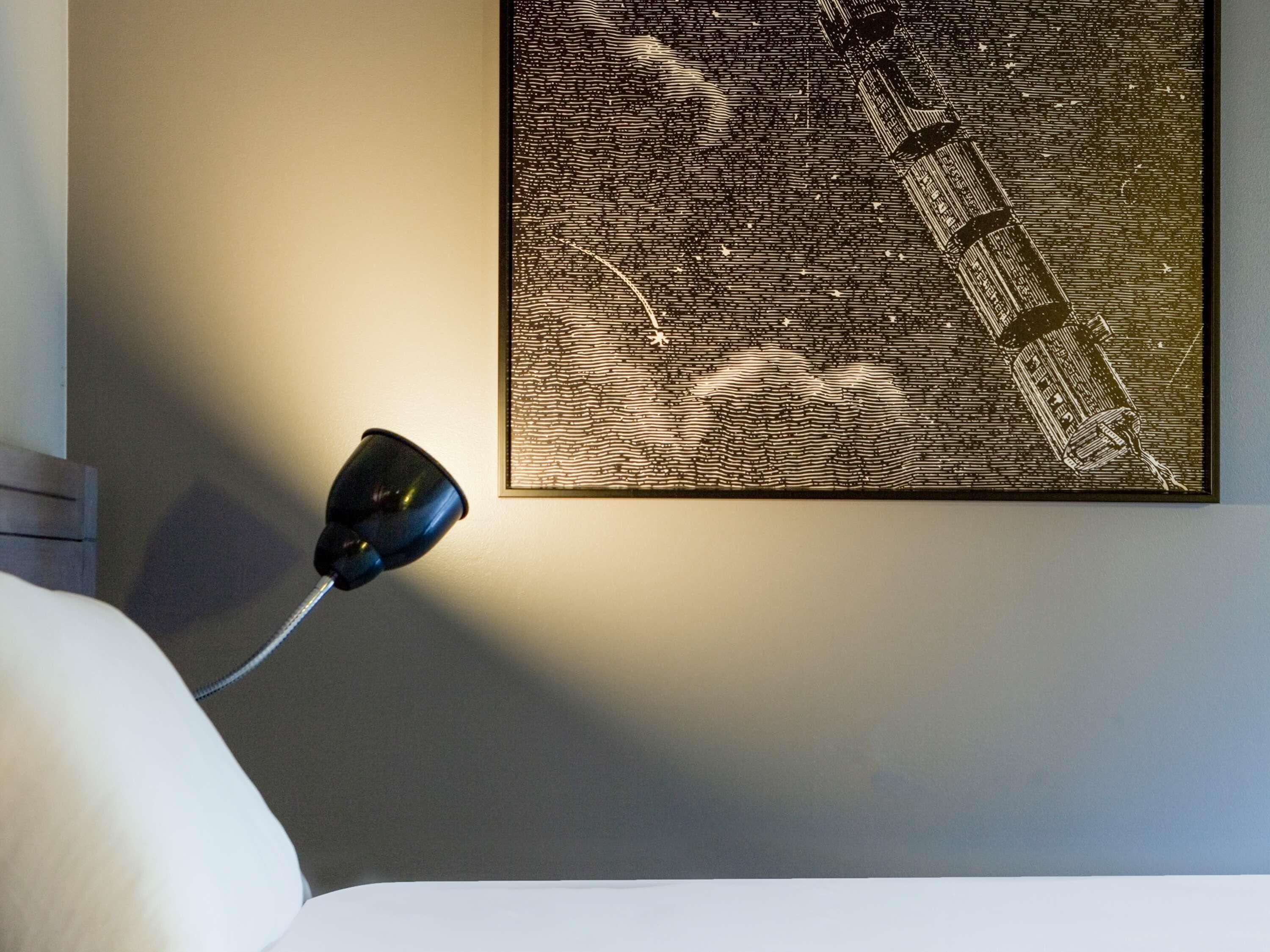 A wall-mounted artwork with a textured pattern, a lamp, and a bed.