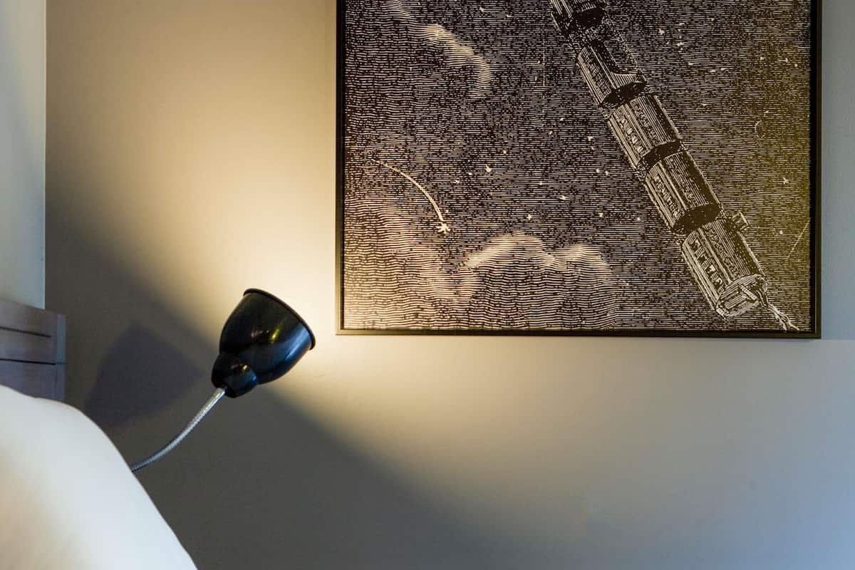 A wall-mounted artwork with a textured pattern, a lamp, and a bed.