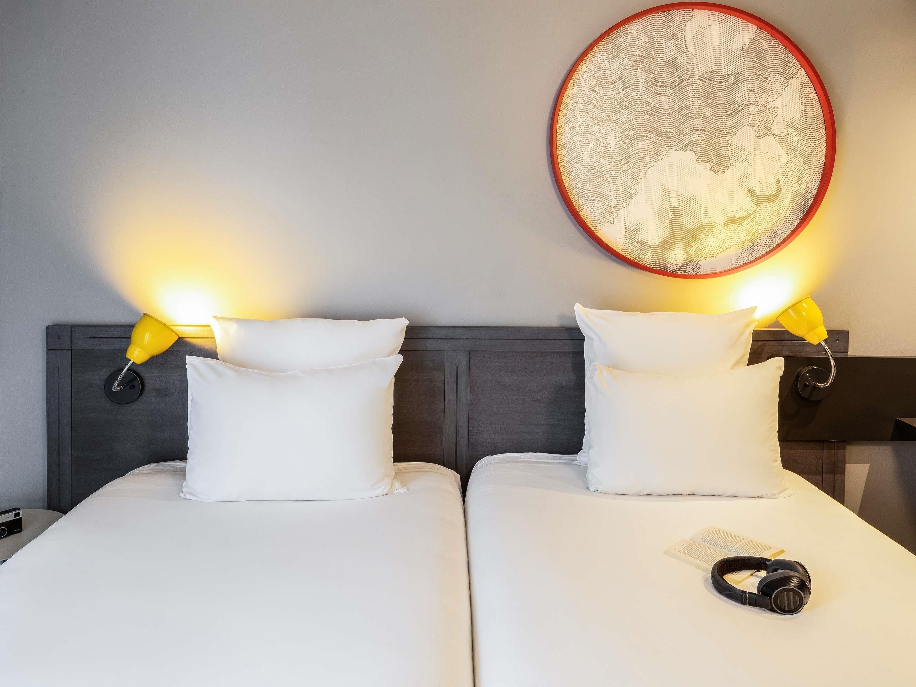 Une chambre d’hôtel avec deux lits, chacun agrémenté de draps et d’oreillers blancs, et une décoration murale ronde au-dessus.