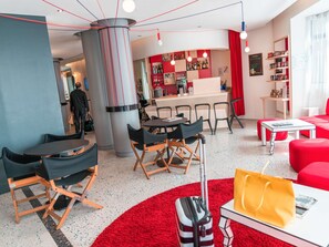 Un hall d’hôtel moderne doté d’un bar, de différents espaces aménagés pour s’asseoir et d’un tapis rouge.