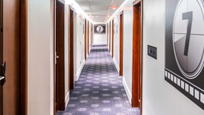 Een hotelgang met vloerbedekking, houten deuren en een groot bord met het cijfer 7 aan de muur.