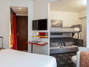A hotel room with a bunk bed, a desk with a flat-screen TV, a small table with a bottle and glasses, and a bed with a white comforter. - ibis Styles Paris Mairie de Montreuil (Montreuil)