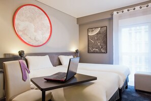 Ein Hotelzimmer mit einem Bett, einem Laptop auf einem Tisch, einem Sessel und Bildern an den Wänden.