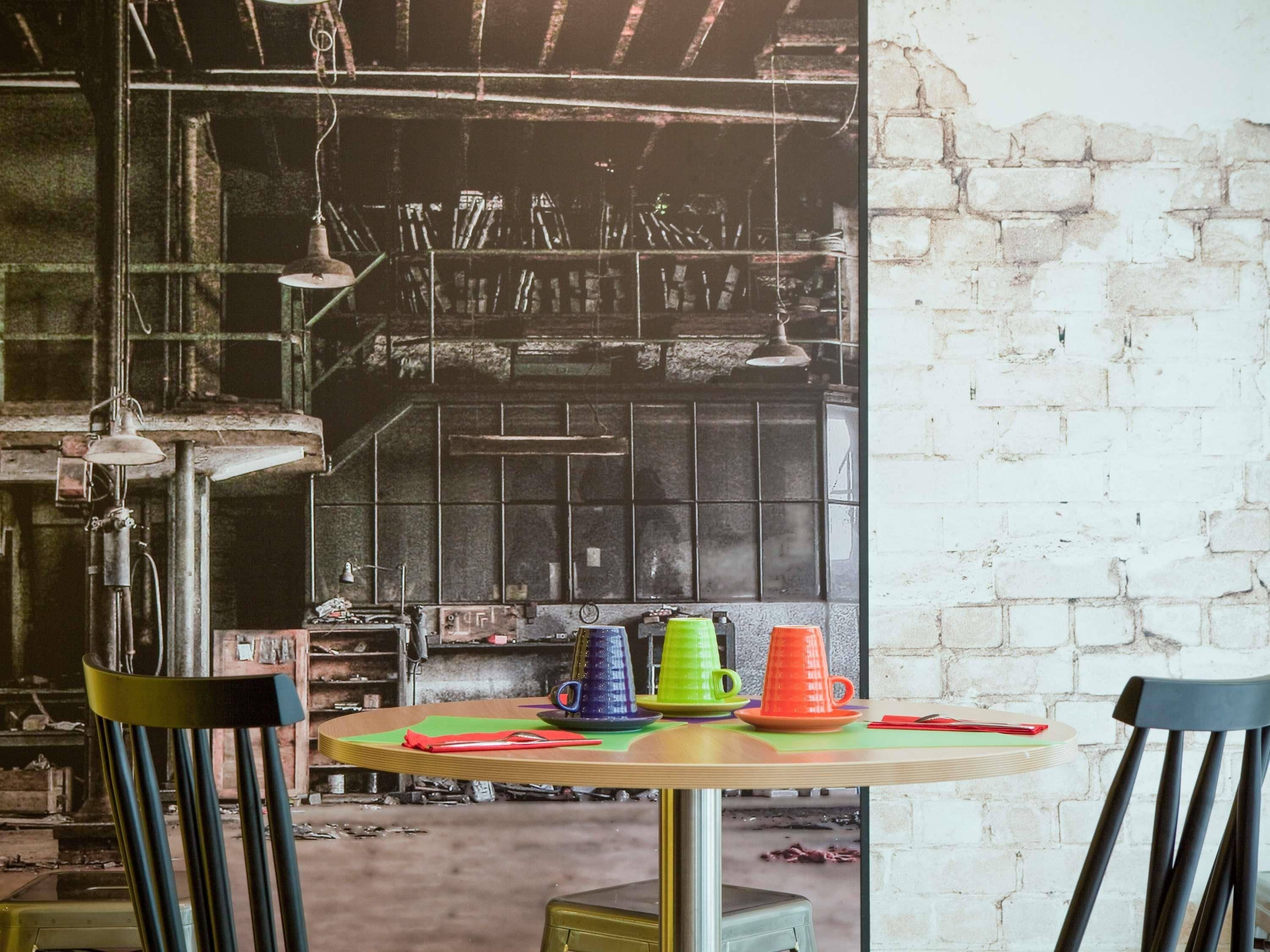 A round table with colorful cups and a chair in a rustic room with exposed brick walls and industrial elements.