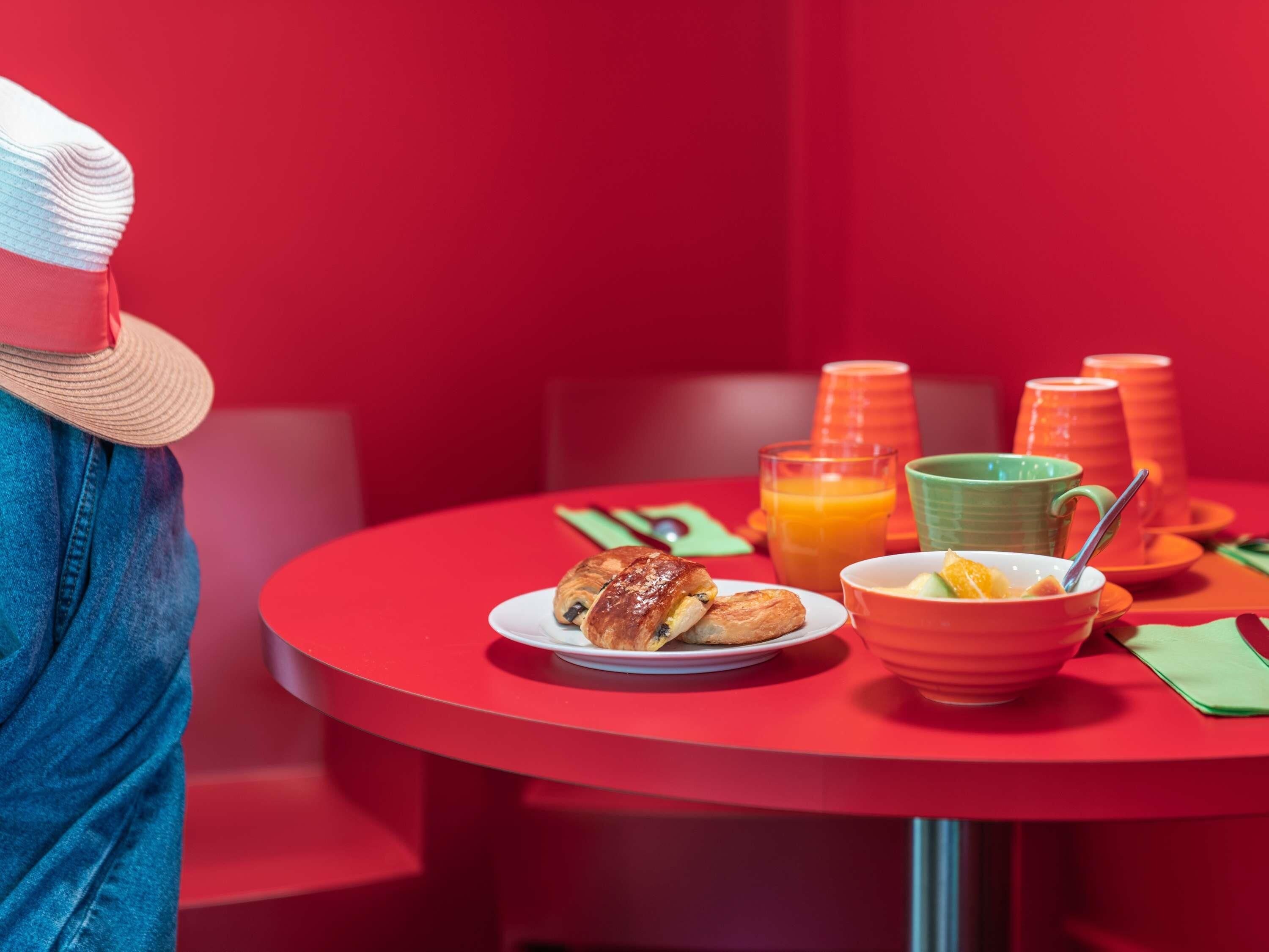 A red table with breakfast items including croissants, a bowl of fruit, and orange juice.