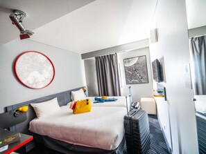 Ein Hotelzimmer mit Bett, Schreibtisch, Stuhl, Koffer und einem Fenster mit Vorhängen.