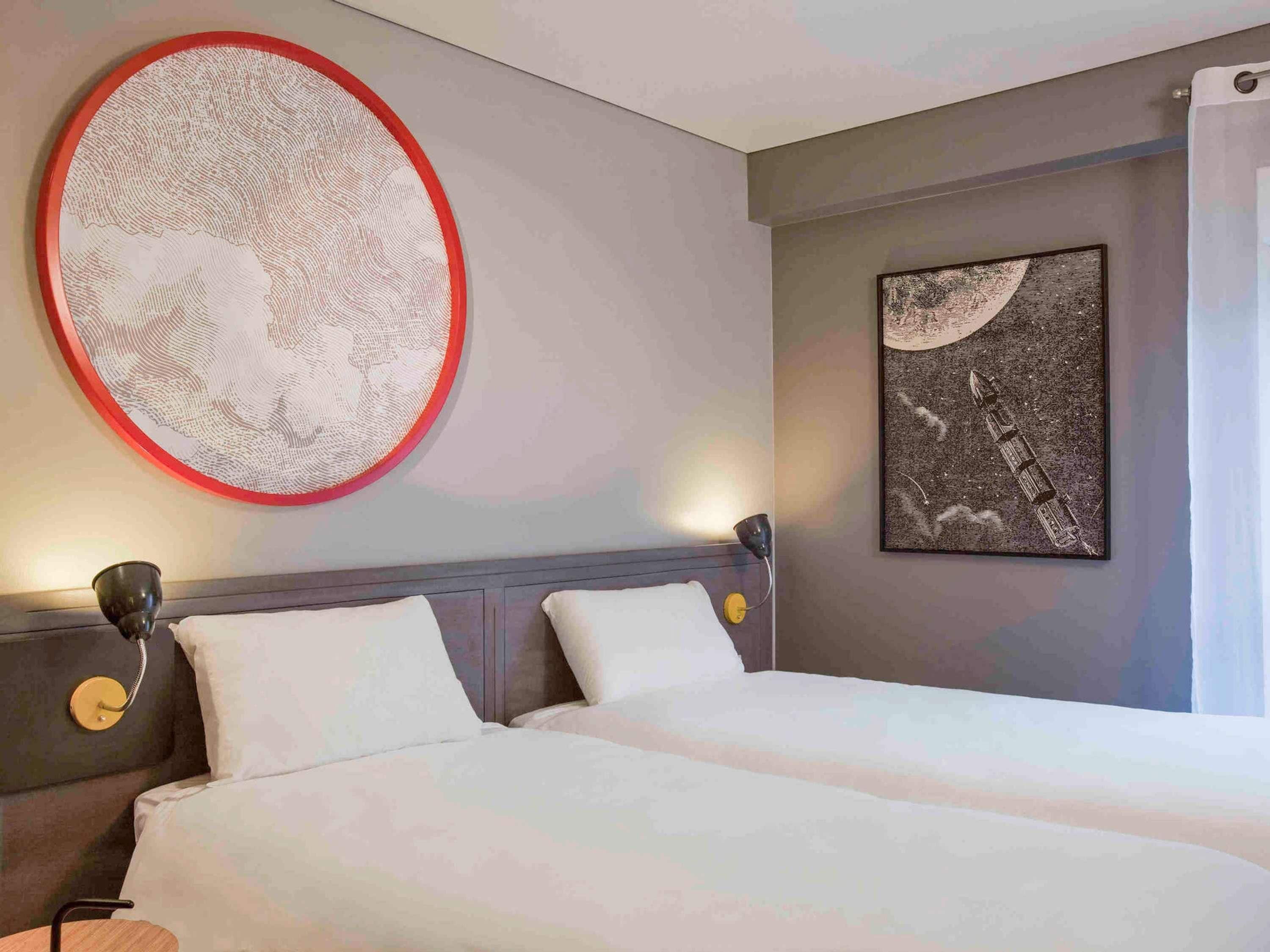 A hotel room with a bed, a headboard, a wall-mounted artwork, a bedside table, and a lamp.