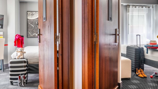Een hotelkamer met een houten garderobe, een bed, een koffer en een bureau met een computer.