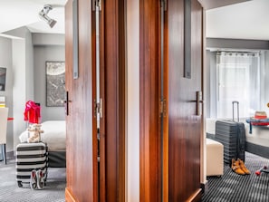 Hotellihuone, jossa on puinen vaatekaappi, sänky, matkalaukku ja työpöytä, jossa on tietokone.