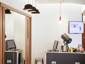 A modern reception desk with a computer, a small stool, and a coffee machine. There is a television screen displaying a service offer. - ibis Styles Paris Mairie de Montreuil (Montreuil)