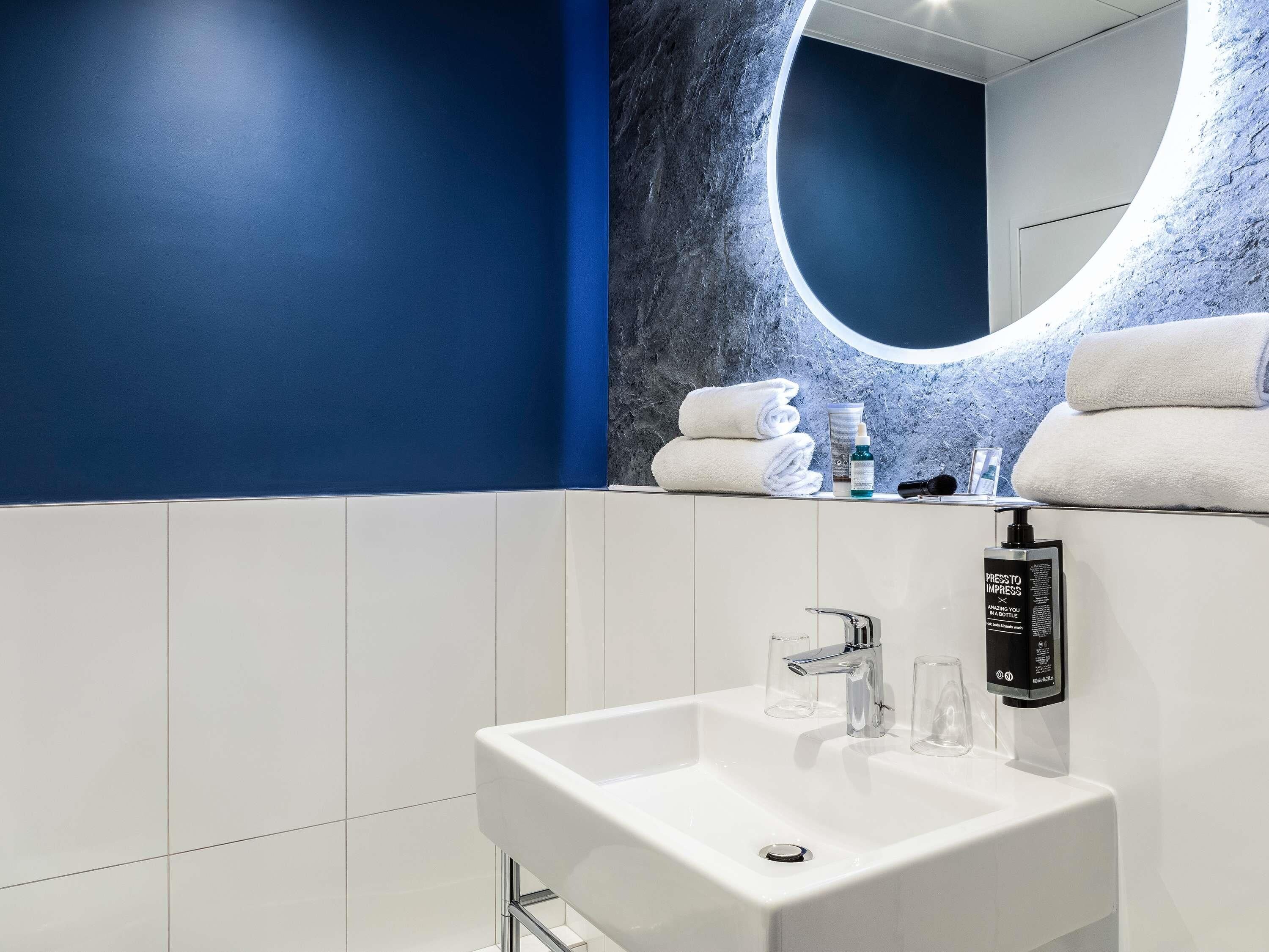 A modern bathroom with a white sink, a mirror with a circular frame, and a blue accent wall.