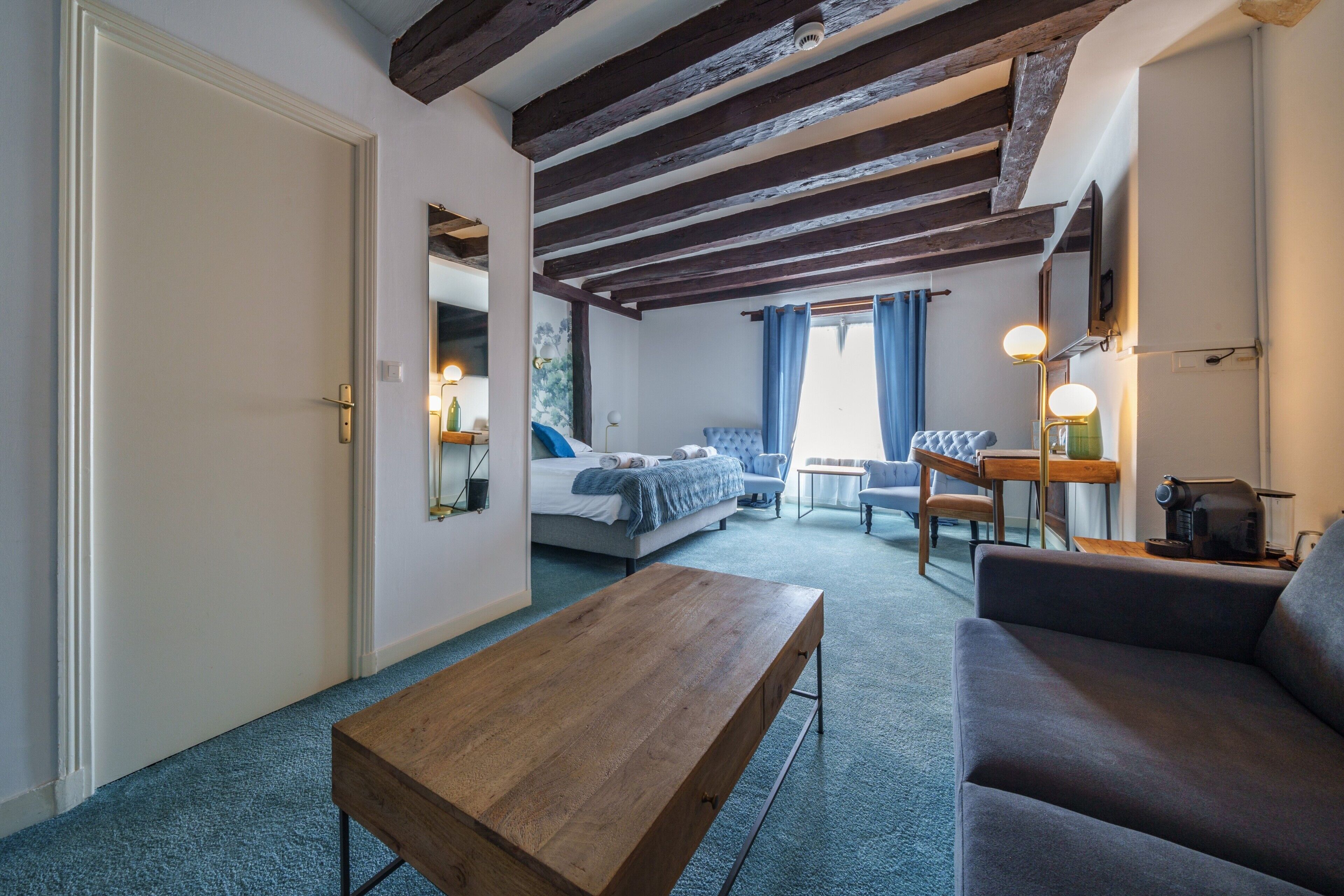 Una habitación con un banco de madera, un sofá, una cama, una mesa y un espejo.