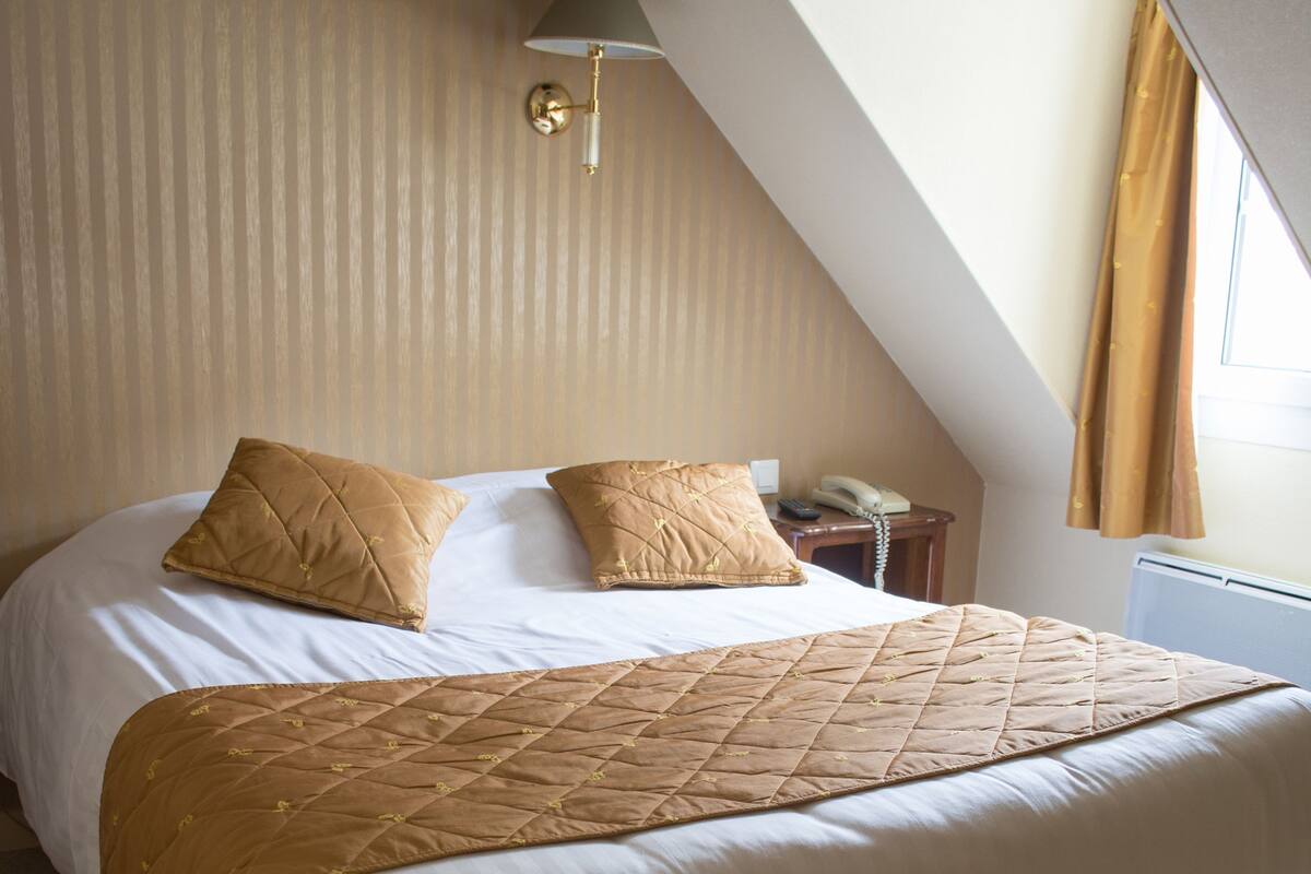 A bedroom with a large bed, a nightstand, a lamp, and a window with curtains.
