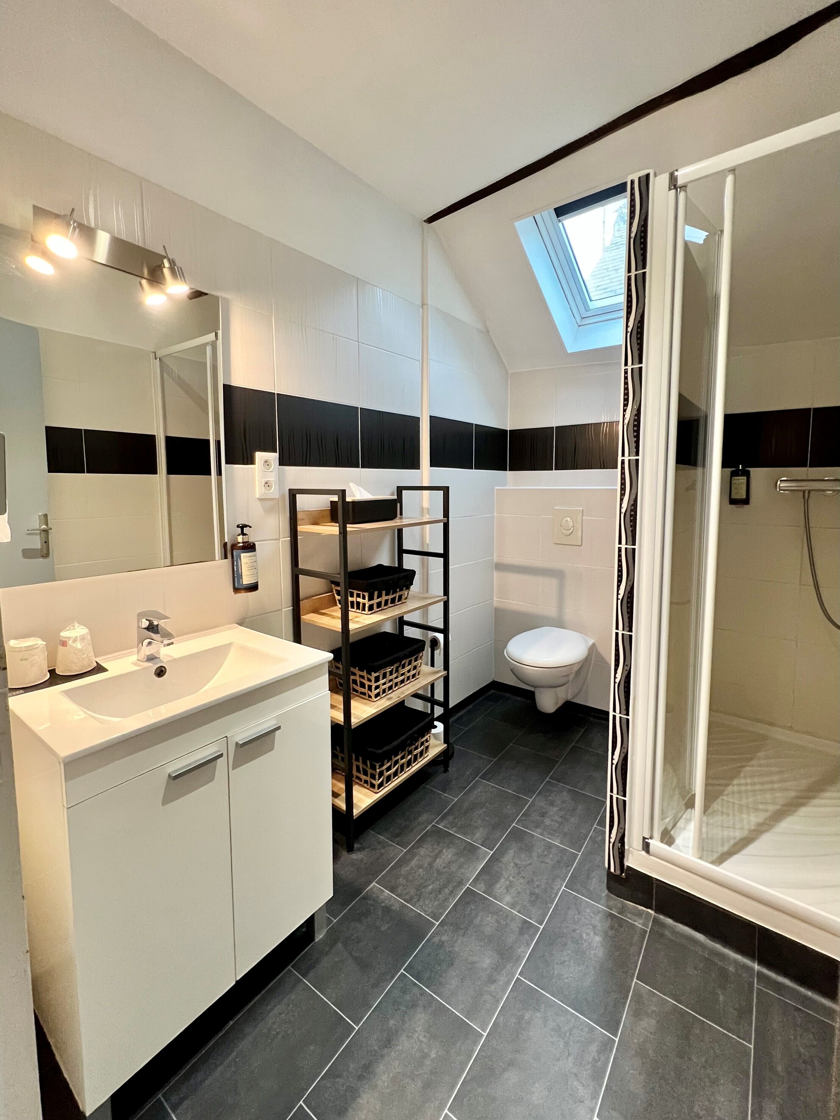 Un baño moderno con tragaluz, un lavamanos blanco, paredes con azulejos blanco y negro, y una zona de ducha.