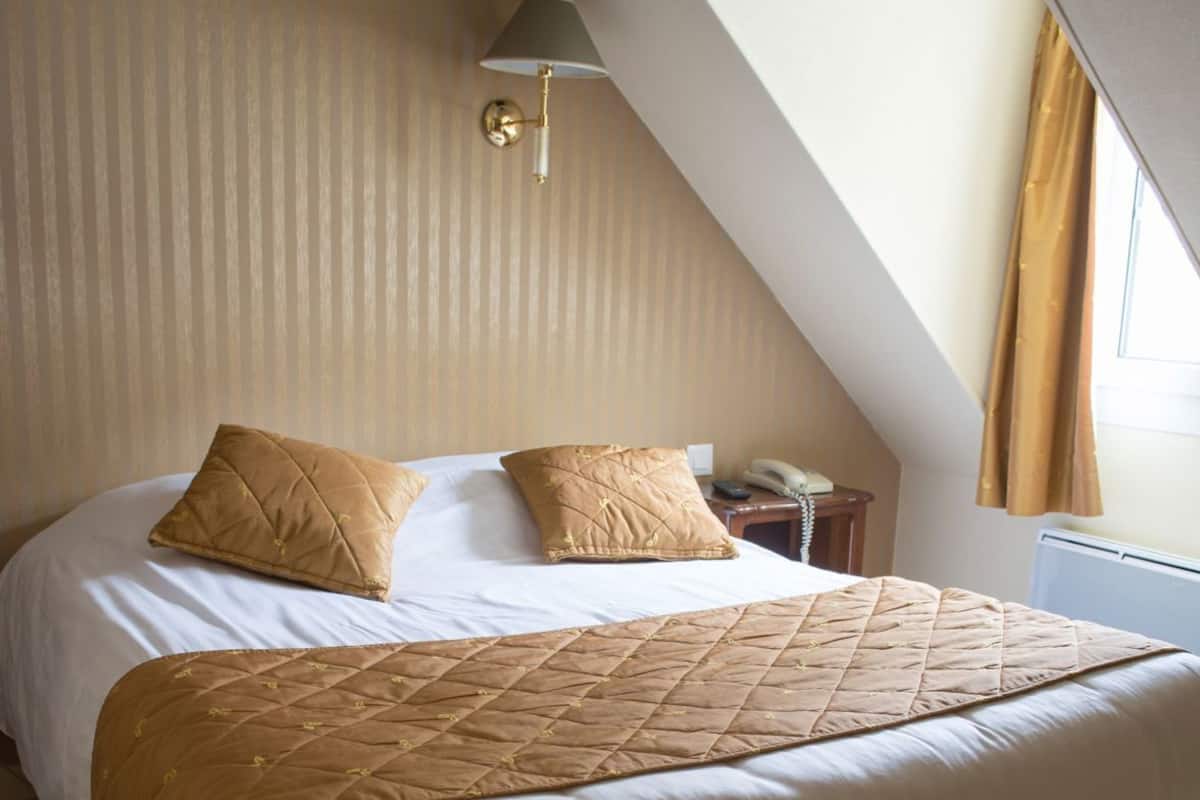 A bedroom with a bed, two pillows, a bedside table with a lamp, and a telephone.