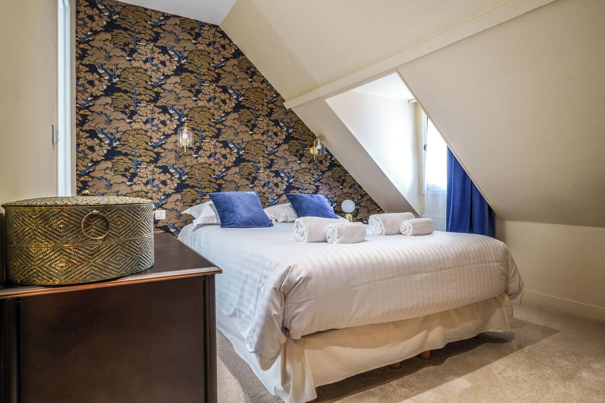A bedroom with a large bed, a nightstand, a decorative lamp, and a patterned wall.