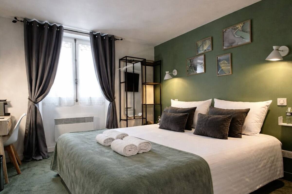 A neatly made bed with rolled towels, a desk with a chair, and artwork on the walls.