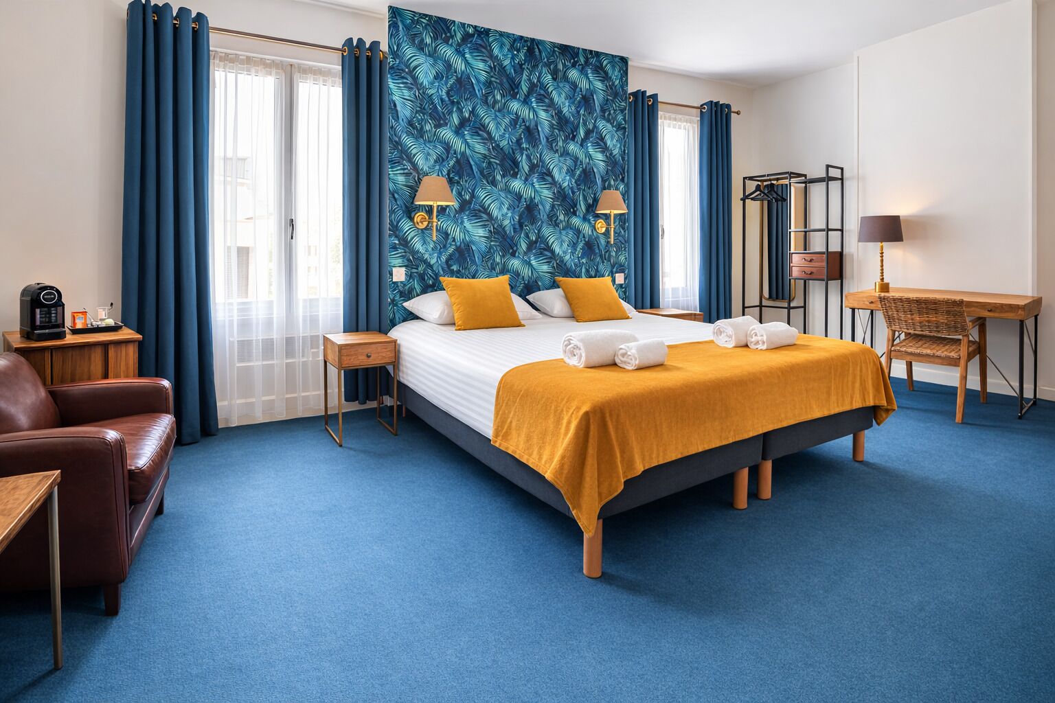 A hotel room with a large bed, a desk, a chair, a coffee machine, and a wardrobe.