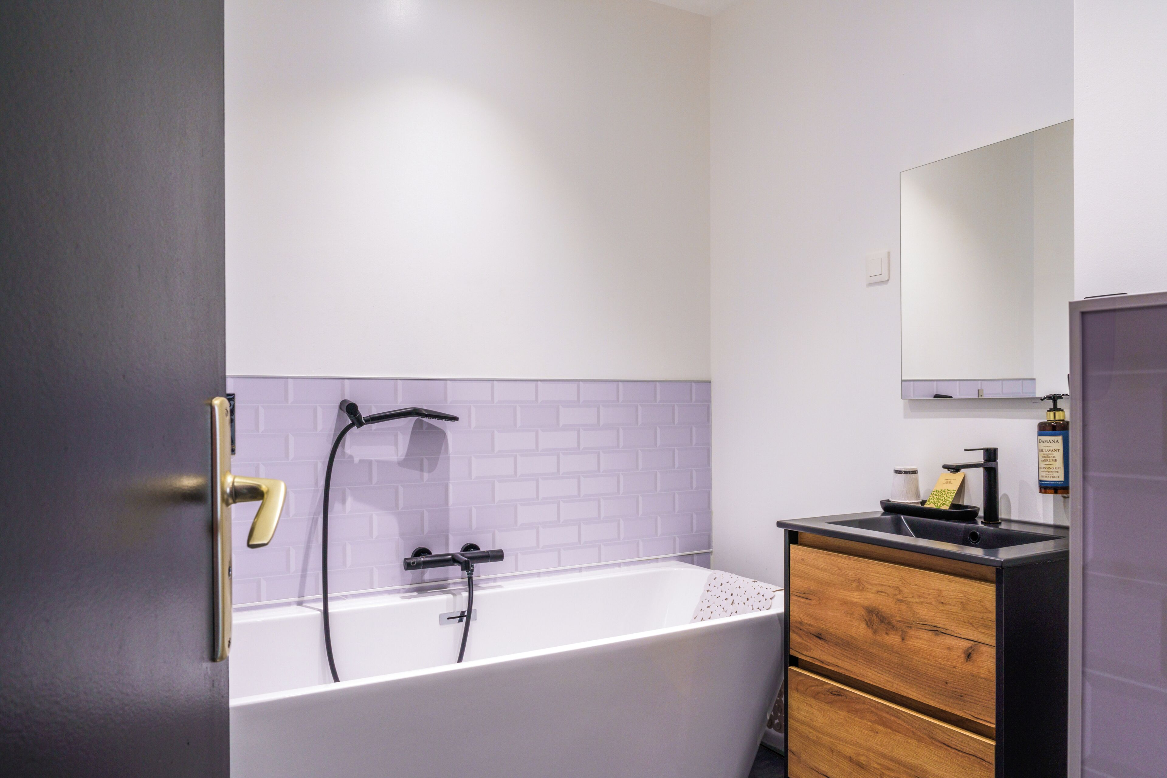 A modern bathroom with a white bathtub, a wooden vanity, and a mirror above the sink.