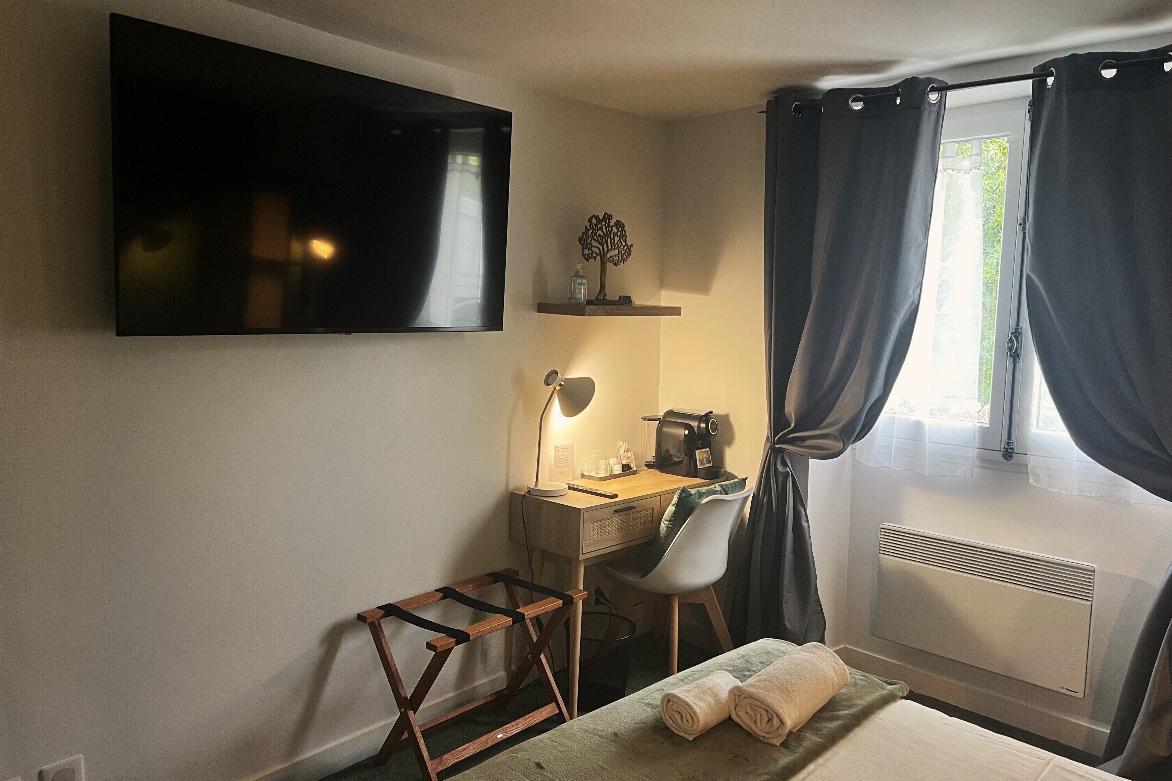Une chambre à coucher comprenant un lit, un bureau avec une chaise, un téléviseur, un radiateur et une fenêtre avec des rideaux.