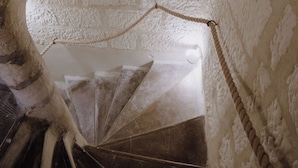A spiral staircase with a rope barrier, leading to a small circular opening in a stone wall. - The Originals Boutique, Hôtel Le George, Loches (Loches)