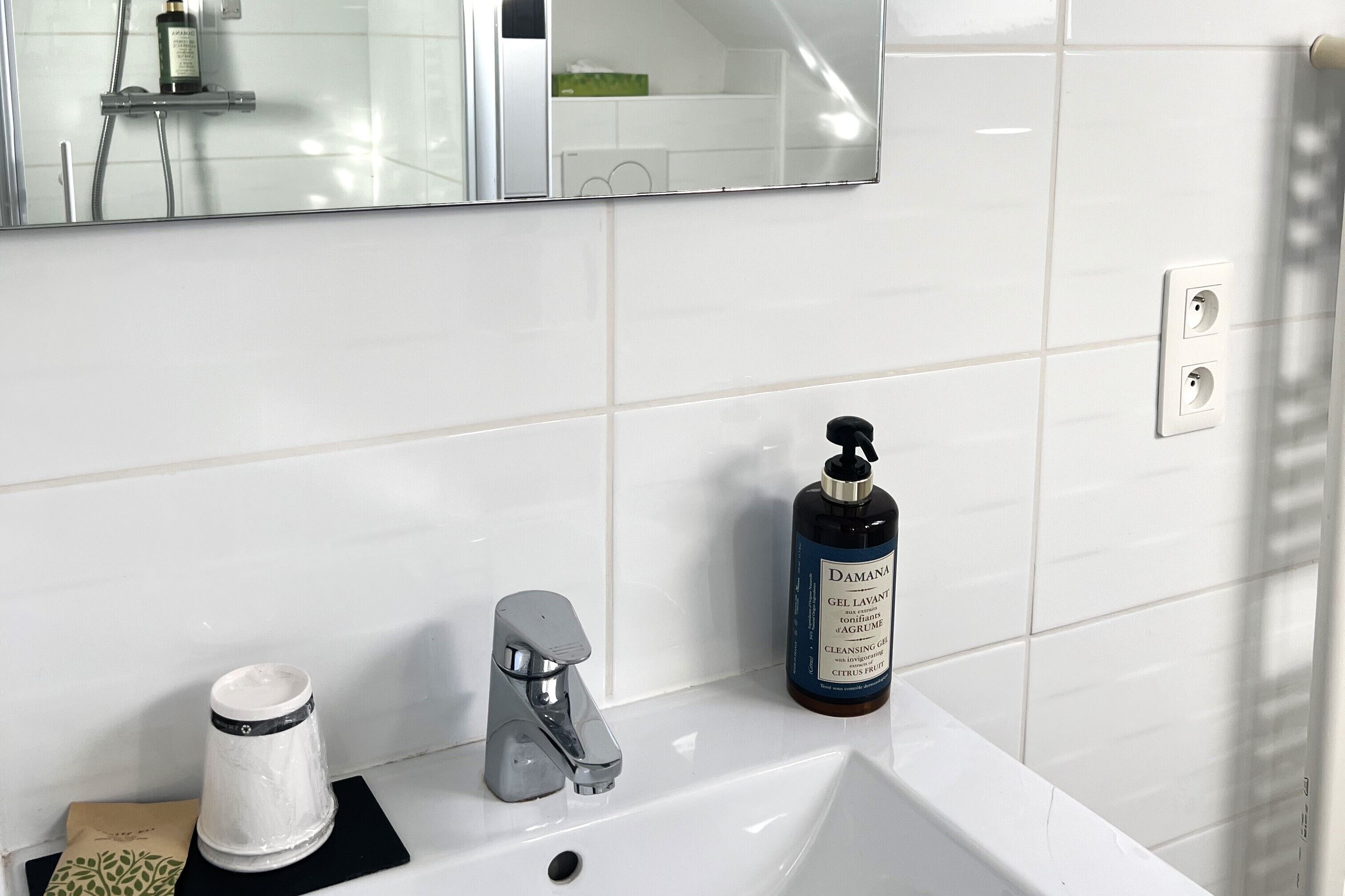 A bathroom with a white sink, a mirror, and a bottle of shampoo.
