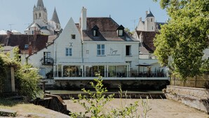 A hotel with a balcony overlooking a canal, historic buildings in the background, and a sign indicating it is a hotel bar restaurant. - The Originals Boutique, Hôtel Le George, Loches (Loches)
