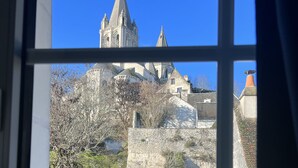 A view of a historic building with a prominent tower and multiple spires, viewed through a window with a grid pattern. - The Originals Boutique, Hôtel Le George, Loches (Loches)