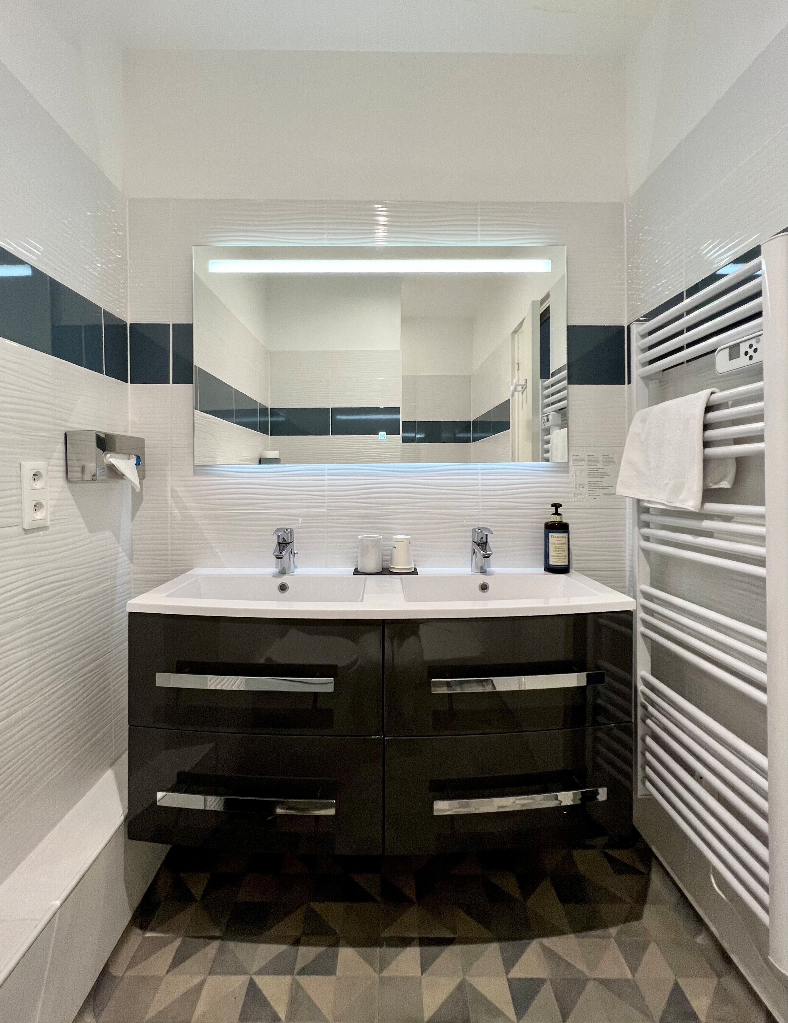 Une salle de bain moderne avec un meuble-lavabo noir et blanc, un grand miroir et un porte-serviettes.