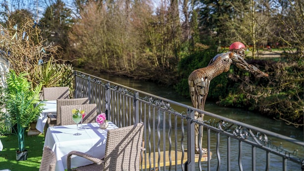 An outdoor dining area with wicker furniture and a table set for two, overlooking a river and surrounded by trees. - The Originals Boutique, Hôtel Le George, Loches (Loches)