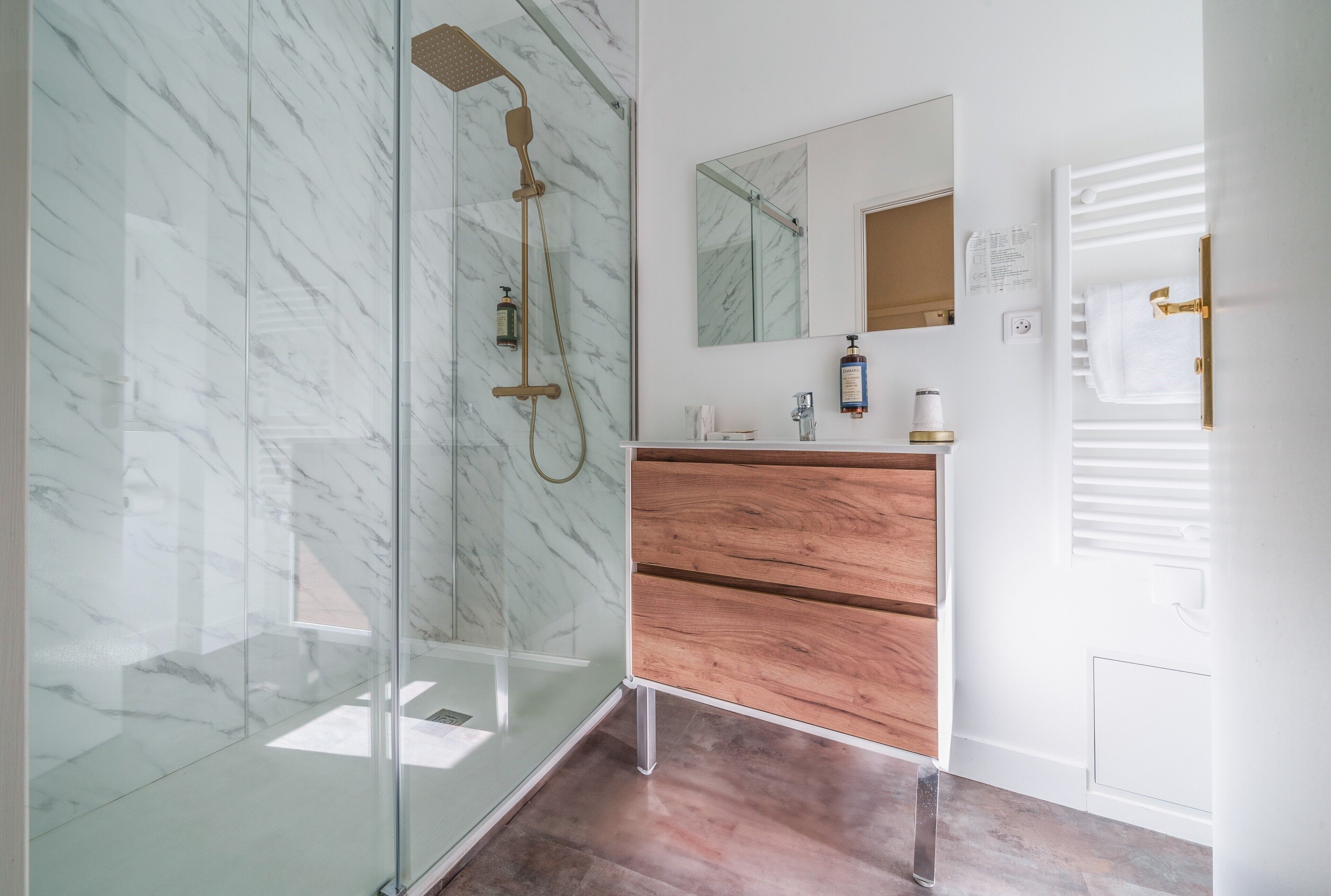 Un bagno moderno con cabina doccia in vetro, mobile lavabo in legno e parete in marmo.
