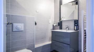 A modern bathroom with grey tiles, a toilet, a sink with a mirror, and a towel dispenser.