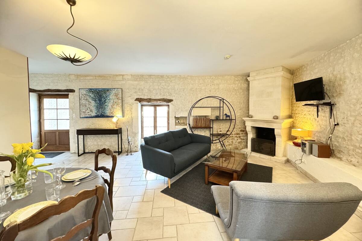 A living room with a sofa, a dining table set, a fireplace, and a TV mounted on the wall.