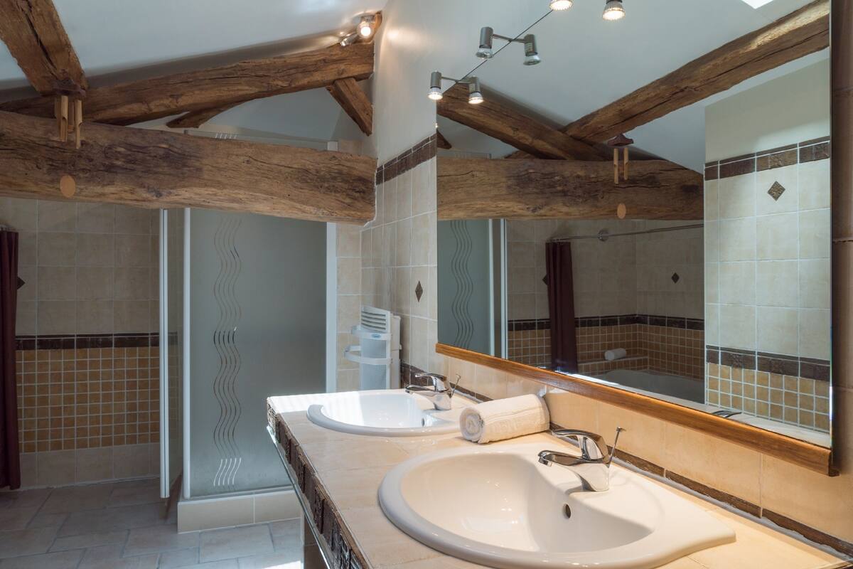 A bathroom with two sinks, a shower, and a large mirror.