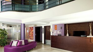 Un vestíbulo moderno con una zona de estar morada curva, una mesa de recepción y una escalera.