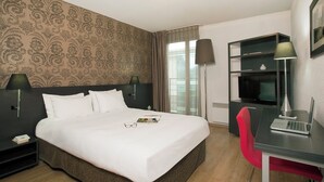 Habitación de hotel con una cama grande, un escritorio con una computadora portátil, una silla roja, un televisor y una estantería.