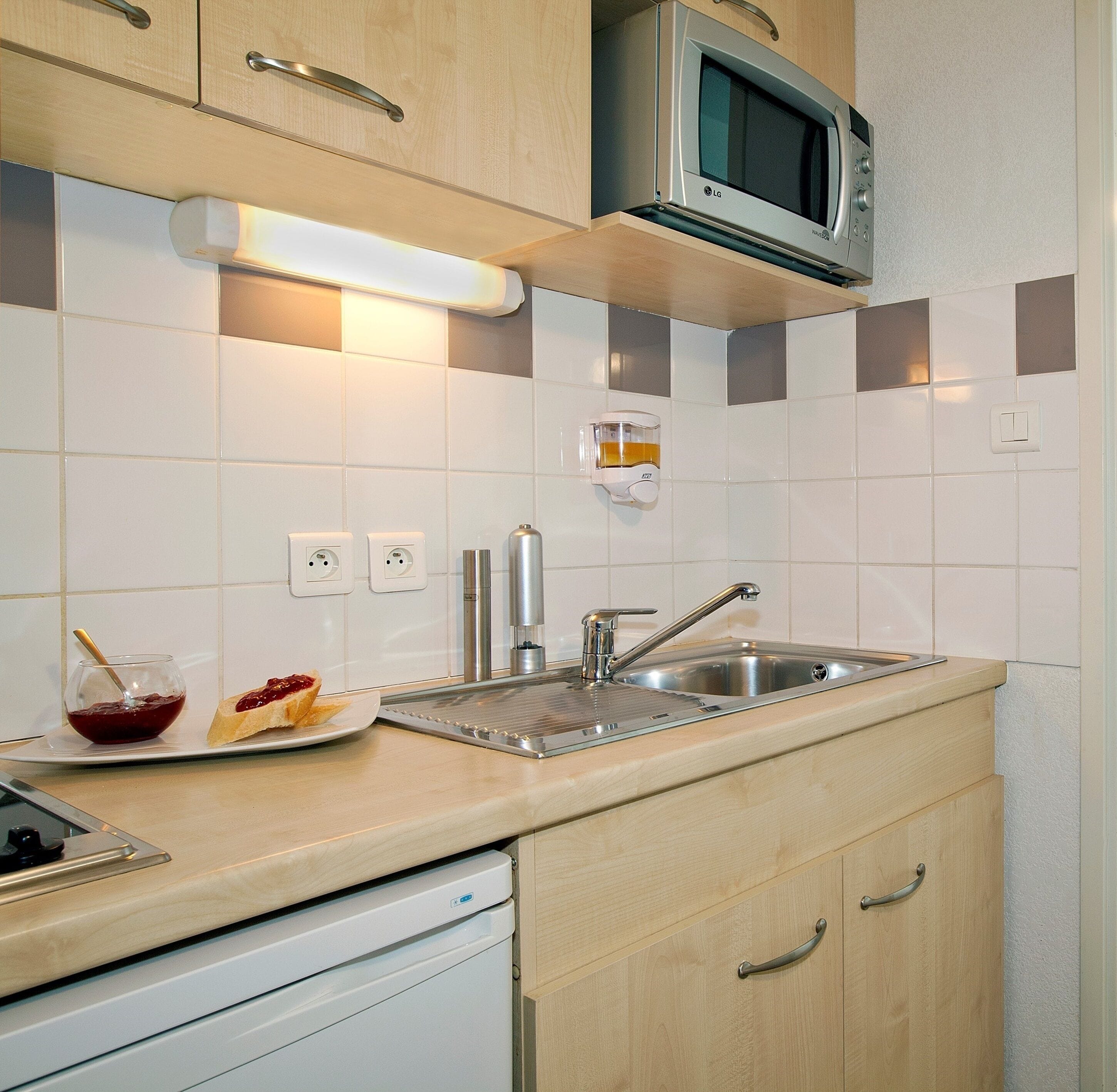 Una cocina moderna con un lavamanos de acero inoxidable, un microondas y un tostador. Hay un plato con tostadas y mermelada sobre la encimera.