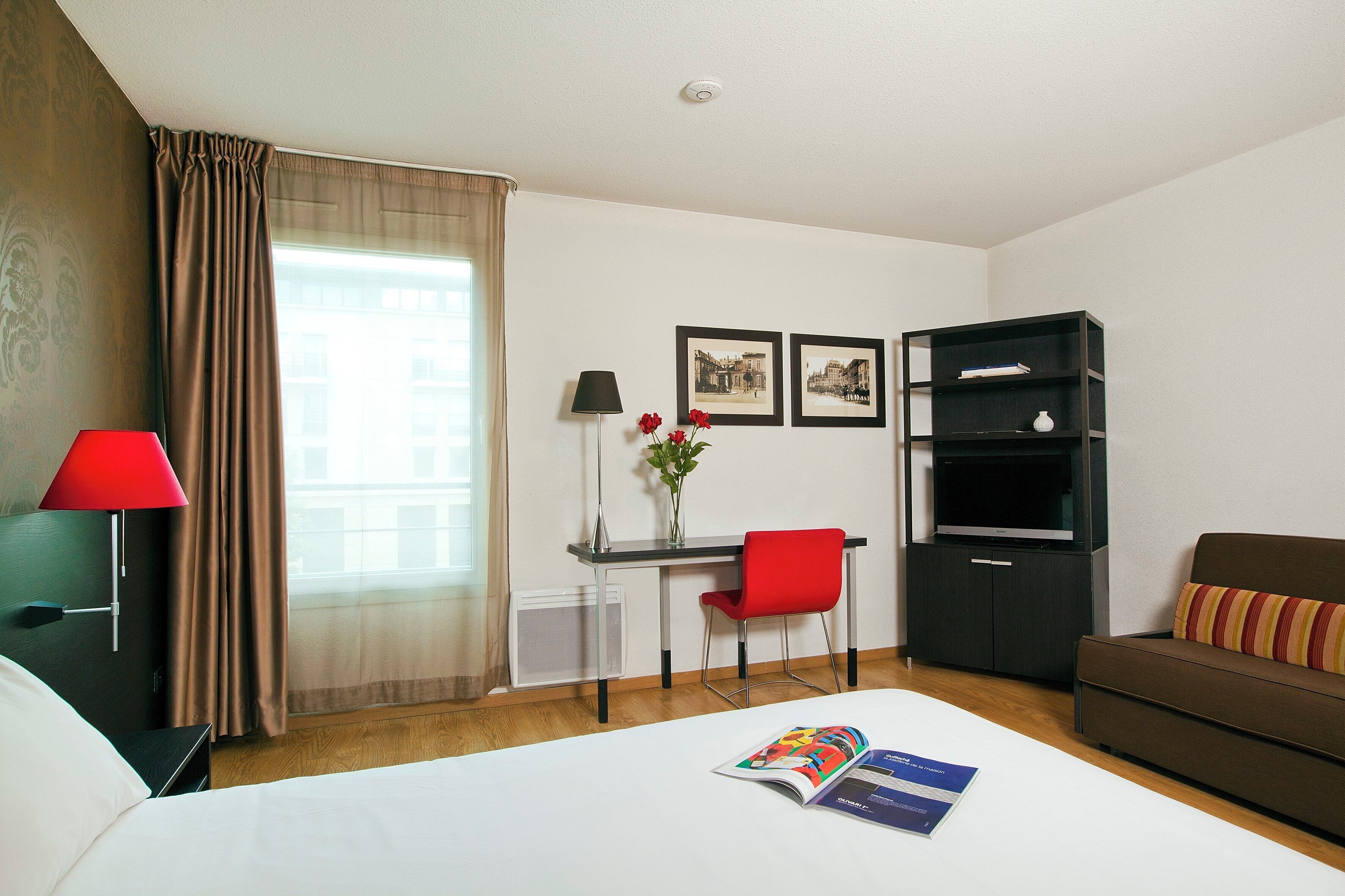 A hotel room with a bed, a desk with a chair, a TV, and a sofa.