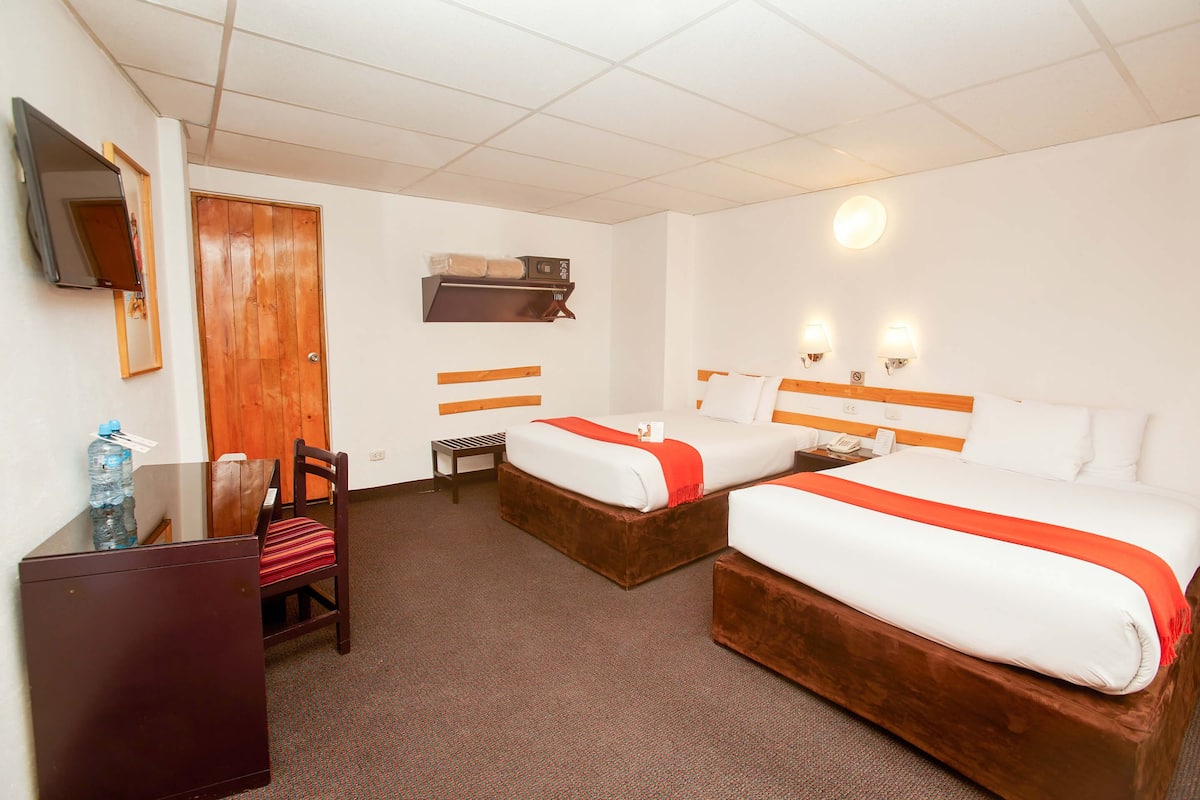A hotel room with two beds, a desk, a chair, a TV, and a bathroom mirror.