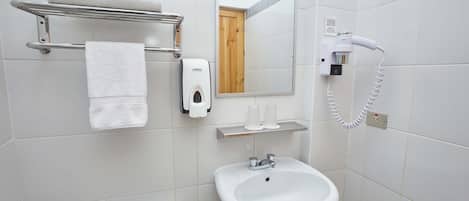 Un baño con lavamanos, espejo, toallero, secamanos y retrete.