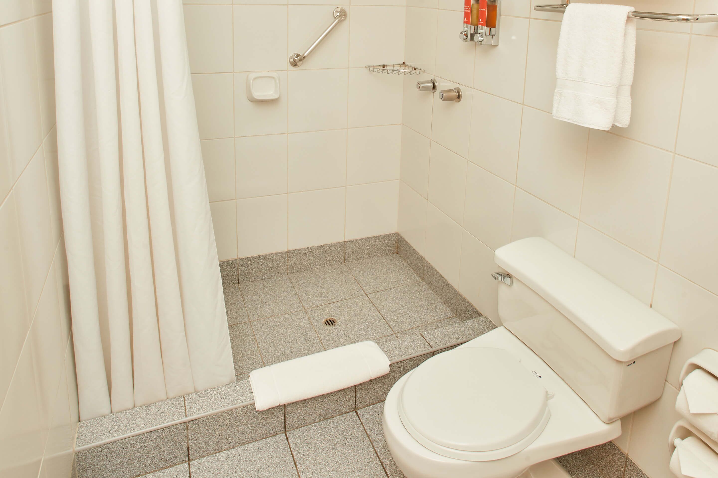 A bathroom with a toilet, a shower curtain, a grab bar, and a towel rack.