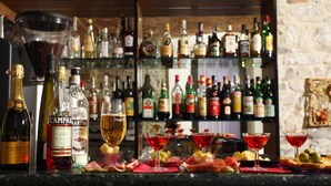 Un bar con una variedad de botellas de licores y vasos, una botella grande de champán, y una selección de aperitivos y bocadillos en la barra.