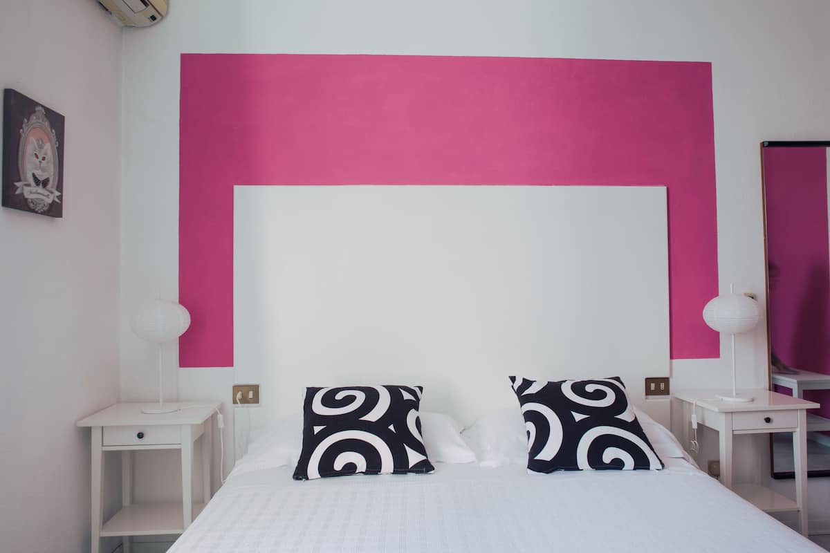A bedroom with a large bed, two bedside tables, a nightstand, a wall-mounted mirror, and a decorative picture frame.