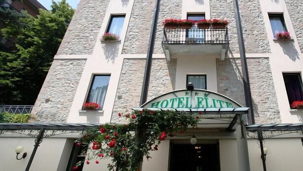 Un hotel con fachada de piedra, un letrero que dice 'HOTEL ELITE' y macetas con flores en las ventanas.